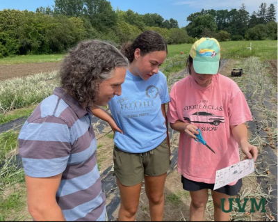 Photo of three people in a field discussing an item on a piece of paper.
